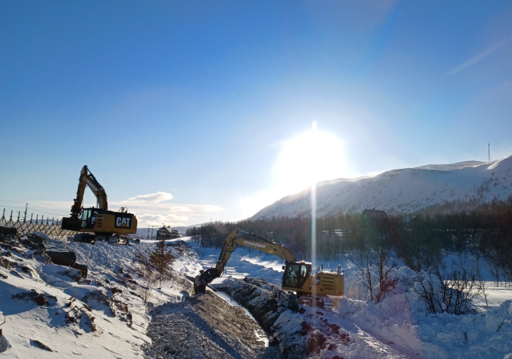 to gule gravemaskiner jobber i veikanten om vinteren med sol og blå himmel